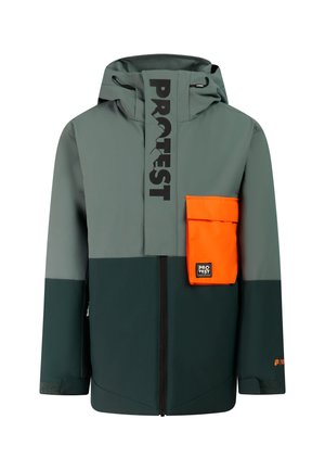 Jongen staat en draagt een groene en grijze jas met een oranje zak, oranje broek, zwarte handschoenen, zwarte laarzen en een zwarte gebreide muts.