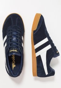 Baskets en daim bleu marine avec rayures blanches et semelle en caoutchouc couleur gomme. Elles présentent un bout rond, un laçage à l'avant et un logo contrastant sur la languette.