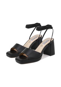 Sandali neri con tacco alto, punta aperta e fascia larga. Presentano un tacco quadrato e sottili lacci per la caviglia, realizzati in pelle liscia.