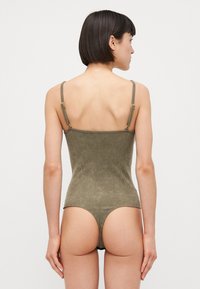 Maillot de bain une pièce côtelé vert olive avec des fines bretelles et un dos dégagé. Présente une coupe échancrée au bas. Texture lisse.