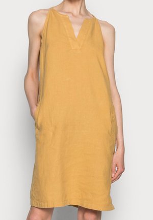 Sleeveless mustard yellow linen dress with V-neck and side pockets worn by a standing person against a plain background.