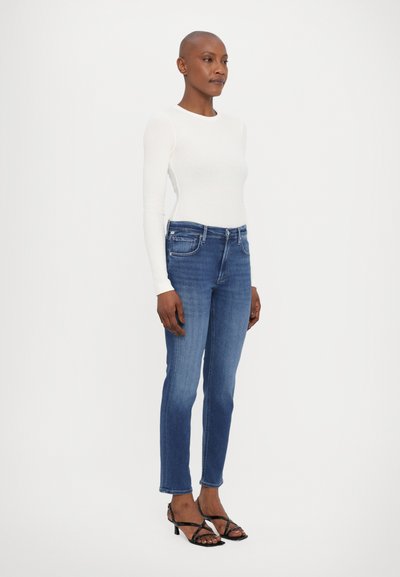 Gestreepte witte lange mouwen top gecombineerd met blauwe denim jeans; de jeans hebben een klassieke pasvorm en een lichte vervaging, aangevuld met zwarte sandaaltjes met banden.