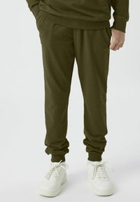 Olivgröna sweatpants med elastisk midja och muddar, tillverkade av mjukt tyg. Matchas med vita snörskor för en avslappnad look.