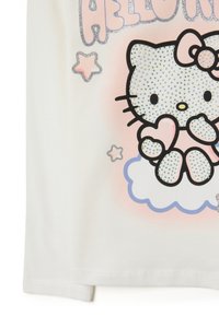 Witte katoenen shirt met een grafisch ontwerp van een personage met een boog, omringd door sterren en een wolk, versierd met glitter en rhinestones.