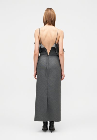 Robe longue grise avec un dos nu, des volants et des bretelles fines. Tissu structuré et sur mesure avec une silhouette droite et une fente latérale.