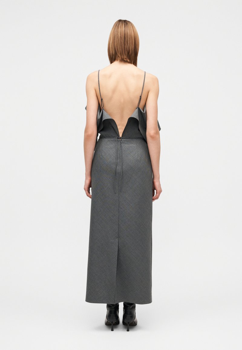 Robe longue grise avec un dos nu, des volants et des bretelles fines. Tissu structuré et sur mesure avec une silhouette droite et une fente latérale.