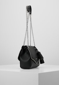 Borsa a tracolla in pelle trapuntata nera con catena argentata, borchie decorative e un accento a nappina. Design squadrato con chiusura a patta.