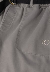 Pantalones cortos de tela gris con acabado texturizado, con un bolsillo frontal y detalle bordado "10". Cinturilla negra con tira ajustable.