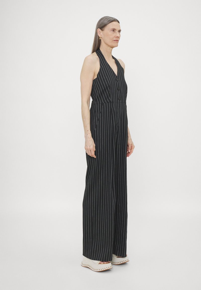 Svartstripet jumpsuit med halterneck, frontknapper og vide ben. Stoffet ser glatt ut, og designet har vertikale hvite striper.