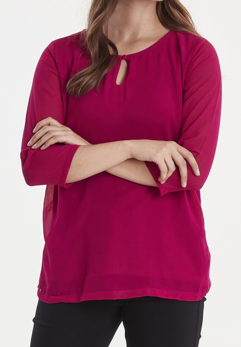 Blusa fucsia con maniche a tre quarti, scollo rotondo e dettaglio a chiave. Tessuto leggero con una texture liscia e una vestibilità comoda.
