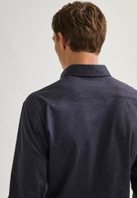 Camicia a maniche lunghe blu navy con colletto, realizzata in un tessuto testurizzato e dettagli sul retro.