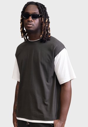 Tume roheline oversized t-särk valgete lühikeste varrukatega. Ümmargune kaelus ja pehme kangas. Kandev isik kannab musti päikeseprille.