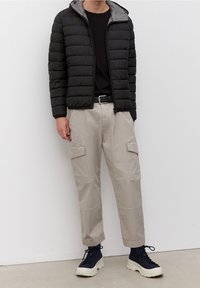 Schwarze, steppierte Pufferjacke mit grauem Futter, kombiniert mit beigen Cargo-Hosen. Zu den Merkmalen gehören Klappentaschen und elastische Bündchen.