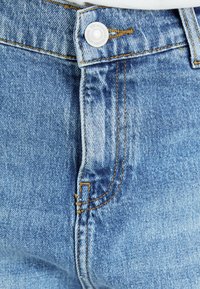 Jeans in denim blu chiaro con cuciture visibili e chiusura a bottone metallico. Il tessuto presenta una leggera texture invecchiata e un classico design a cinque tasche.