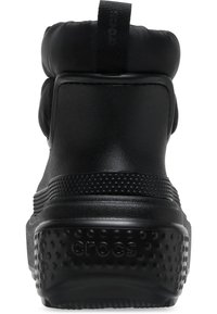 Bota impermeable negra con collar acolchado, suela de goma texturizada y tira de agarre. Cuenta con un acabado suave y un patrón de puntos elevados en la suela.