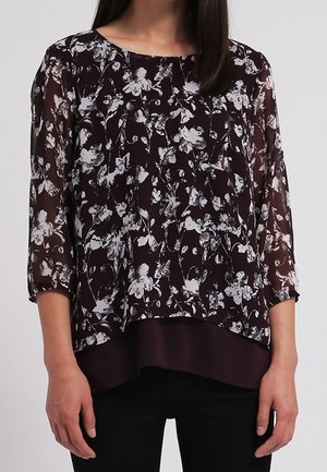 Blusa floreale in bordeaux scuro con maniche lunghe trasparenti, scollatura tonda e orlo stratificato. Caratterizzata da un motivo floreale bianco su tutta la superficie.
