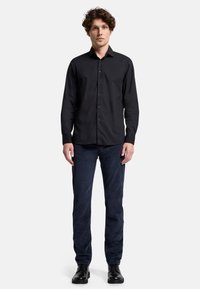 Camicia nera a maniche lunghe con colletto button-down, realizzata in un tessuto leggero e liscio. Abbinata a pantaloni in velluto a coste blu scuro e scarpe nere.