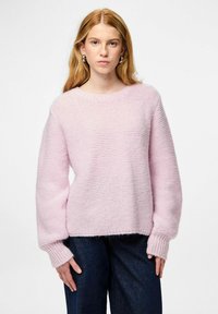 Vaaleanpunainen neulepusero, jossa rento istuvuus, resorit hihansuuissa ja pyöreä pääntie. Yhdistetty tummiin farkkuihin. Kankaan tekstuuri näkyvissä.