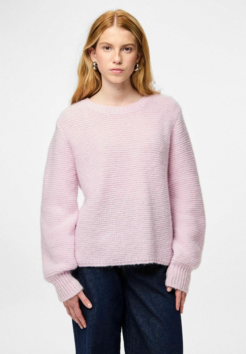 Vaaleanpunainen neulepusero, jossa rento istuvuus, resorit hihansuuissa ja pyöreä pääntie. Yhdistetty tummiin farkkuihin. Kankaan tekstuuri näkyvissä.