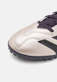 Kovově stříbrné fotbalové kopačky s texturovaným povrchem, černými akcenty a fialovými tkaničkami, s nízkým profilem a tvarovanou gumovou podrážkou.