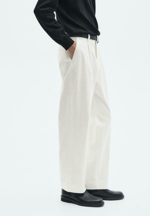 White wide-leg trousers with a smooth texture, worn with a black long-sleeve top and black shoes. Featuring pockets and a classic design.