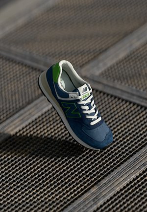 Marineblauwe en groene New Balance 574 sneaker van suede en mesh materialen, met witte veters, logo detail en een gestructureerde rubberen zool.
