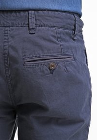 Pantalones de algodón azul marino con un acabado texturizado, que cuentan con un bolsillo trasero con cierre de botón y un lazo para cinturón en la cintura.