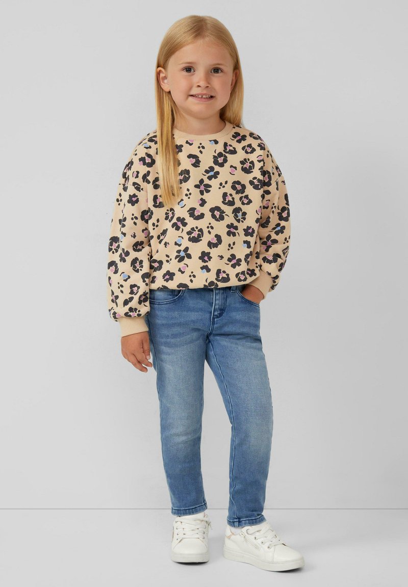 Felpa beige con stampa leopardata nera e rosa, abbinata a jeans skinny blu e sneakers bianche. Tessuto morbido e vestibilità comoda.
