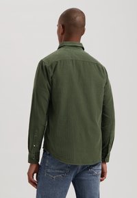 Green long-sleeve shirt with a textured finish, button-up cuffs, and a collar. Worn with blue denim jeans, showing the back view.