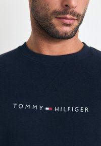 Marine genser med "TOMMY HILFIGER" logo i hvitt med røde og blå detaljer. Rund hals med teksturert finish.