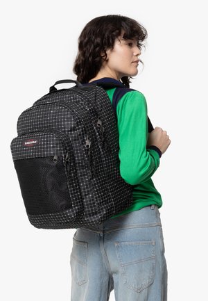 Mochila a cuadros en blanco y negro con bolsillo frontal de malla, doble tirador de cremallera, correas acolchadas y costuras reforzadas.
