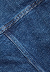 Nahaufnahme von blauem Denimstoff mit diagonal doppelt genähten Nähten mit orangefarbenem Garn und strukturiertem Webmuster.