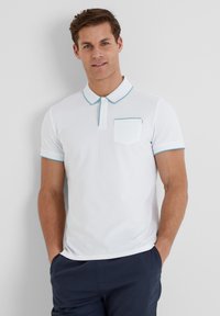 White polo shirt with a collar, teal accent stitching, short sleeves, and a chest pocket. Smooth fabric texture. Worn with navy shorts.
