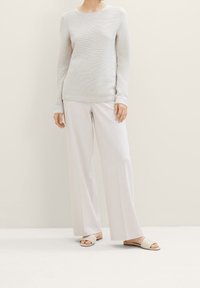 Maglione a maniche lunghe grigio chiaro a coste abbinato a pantaloni larghi di colore crema e sandali beige senza fibbie.