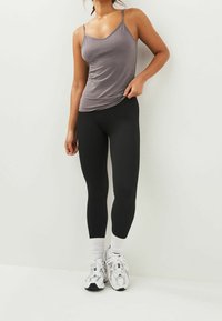 Haut gris sans manches avec des bretelles fines ; leggings noirs côtelés ; chaussettes de sport blanches ; baskets gris et blanches. Design simple et ajusté.