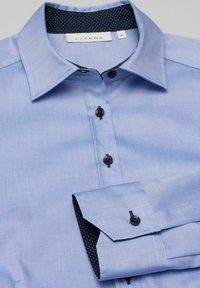 Helles blaues Hemd mit glatter Textur, schwarzen Knöpfen und einem gemusterten navyfarbenen Kragenfutter. Verfügt über ein klassisches Button-Up-Design.