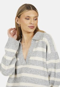 Maglione a righe grigie e bianche con scollatura a V, polsini a costine e texture morbida. Il design ha una vestibilità rilassata con colletto.