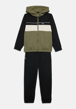Ensemble de survêtement deux pièces avec une veste zippée à capuche, en blocs de couleurs vert olive, noir et blanc, associé à un pantalon noir avec des poignets élastiques.