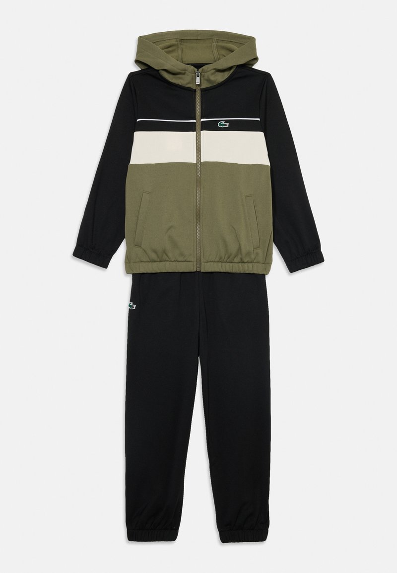 Ensemble de survêtement deux pièces avec une veste zippée à capuche, en blocs de couleurs vert olive, noir et blanc, associé à un pantalon noir avec des poignets élastiques.