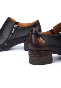 Bottines en cuir noir et marron avec un petit talon, dotées d'une fermeture éclair sur le côté, de panneaux texturés et d'un détail de logo au talon.