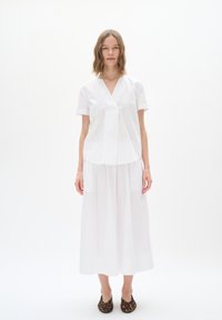 Top bianco a maniche corte con scollatura a V e design plissettato, abbinato a una lunga gonna bianca e mocassini con stampa leopardata. Tessuto liscio, stile minimalista.