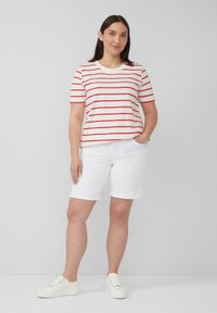 Witte shirt met korte mouwen en rode strepen, gecombineerd met witte opgerolde shorts en witte sneakers. Eenvoudig, casual ontwerp met een ontspannen pasvorm.