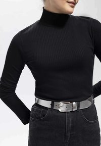 Svart ribbad långärmad topp med hög hals, kombinerad med högmidjade svarta jeans och ett metalliskt silverbälte med en texturerad yta.