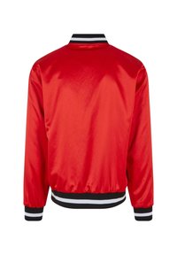 Rød satin bomberjakke med sort og hvid stribet ribbet krave og manchetter. Har elastisk kant og glat tekstur.