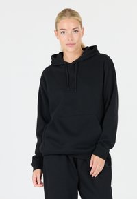 Felpa nera in cotone con cappuccio, cordino, tasca frontale e polsini a coste. Il tessuto ha una consistenza morbida e un design semplice e minimalista.