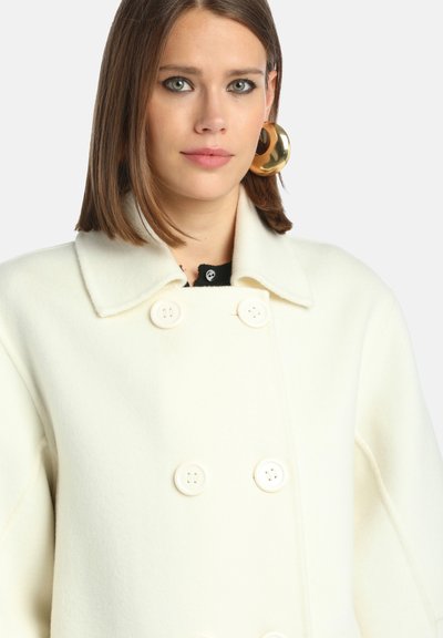 Valkoinen villatakki, jossa on suuret napit, leveä kaulus ja jämäkkä muoto. Sujuva pinta ja räätälöity istuvuus.