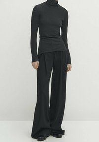 Langærmet, sort turtleneck-bluse i ribbet tekstur parret med løstsiddende, brede sorte bukser. Outfittet har et minimalistisk design.