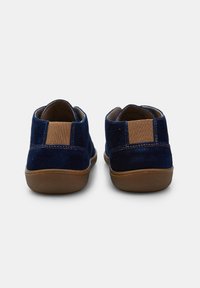 Scarpe in suede blu navy con un pannello elastico marrone al tallone, dotate di punta tonda e suola in gomma marrone chiaro. Texture liscia con cuciture ridotte al minimo.