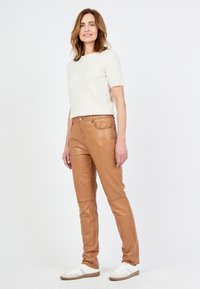 Tan leren broek met een slim fit, hoge taille en subtiele stikdetails, gecombineerd met een lichtbeige T-shirt met korte mouwen en witte sneakers.