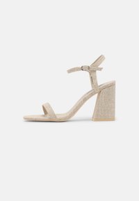 Beige hoge hakken sandalen met een gestoffeerde bovenkant, open teen ontwerp en een slanke enkelband. Stevige, vierkante hak voor stabiliteit.